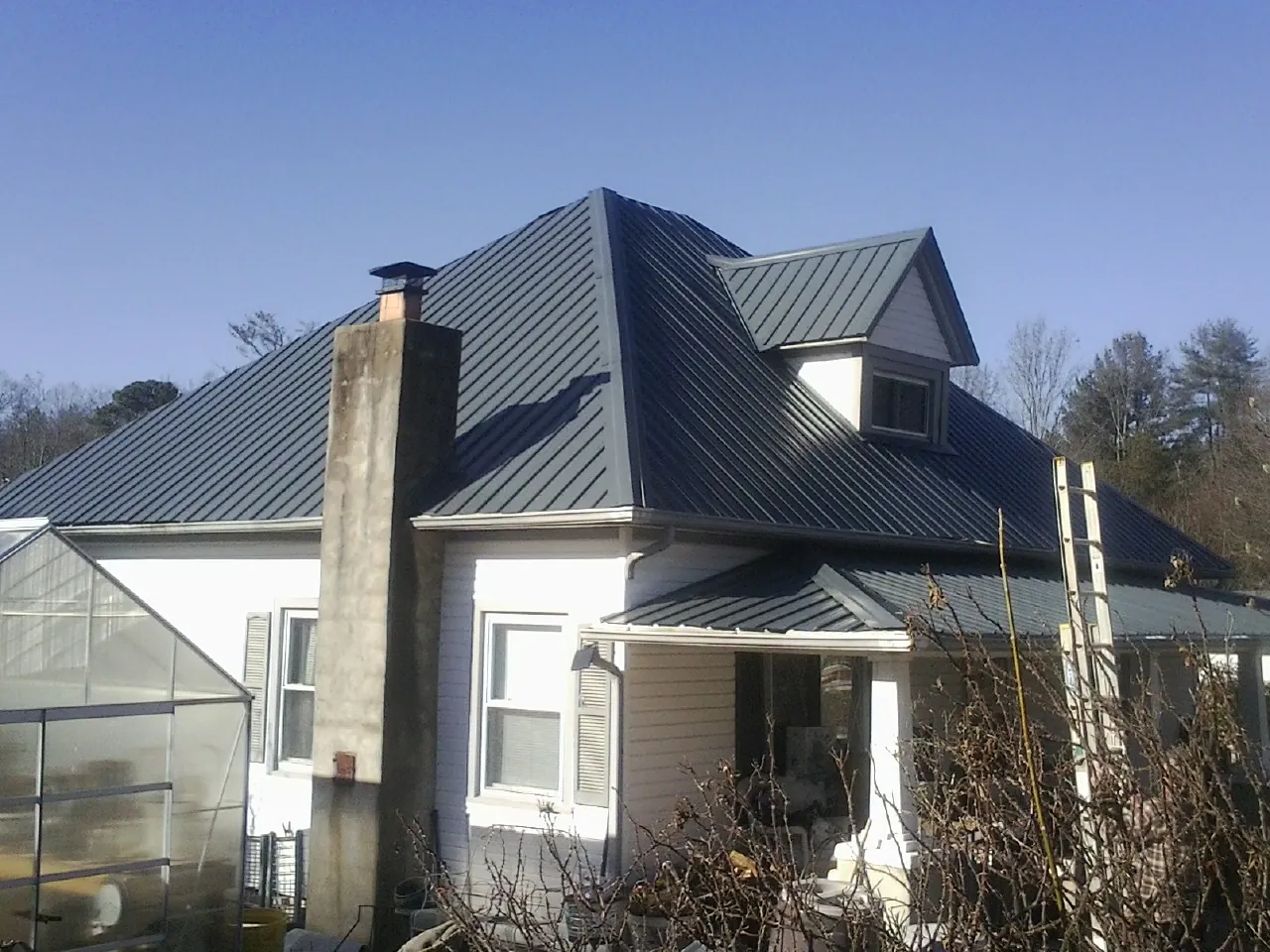 Dark blue standing seam metal roof on a white farmhouse with dormer — Slate & Tile Roof Repair by Roofing Brothers in Crystal City