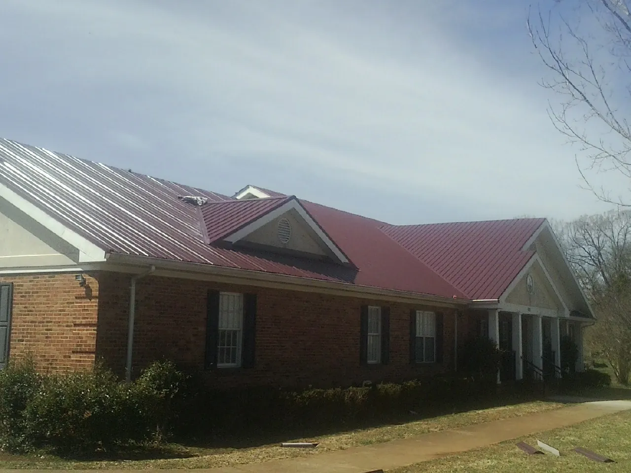 Red metal roof with gabled entries on a long brick building, from a Hail Damage Roof Repair job in Crystal City