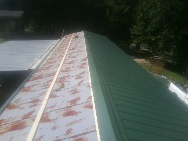 Old rusted panels beside newly installed green metal roofing — Wind Damage Roof Repair by Roofing Brothers in Crystal City