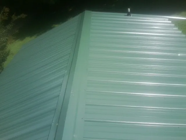 New green metal panels meeting at the ridge of a roof — Flat Roof Repair work by our crew in Crystal City