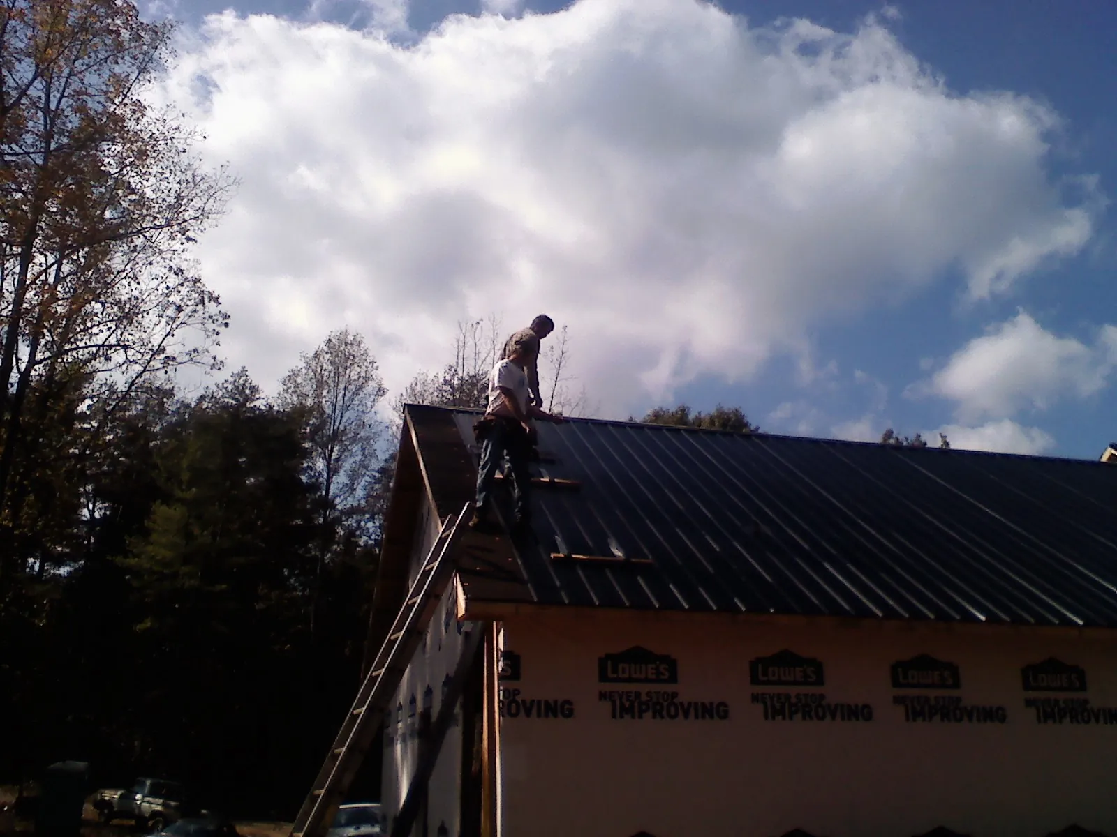Roofer fastening dark metal panels high against a cloudy sky, from a Roof Inspection job in Crystal City