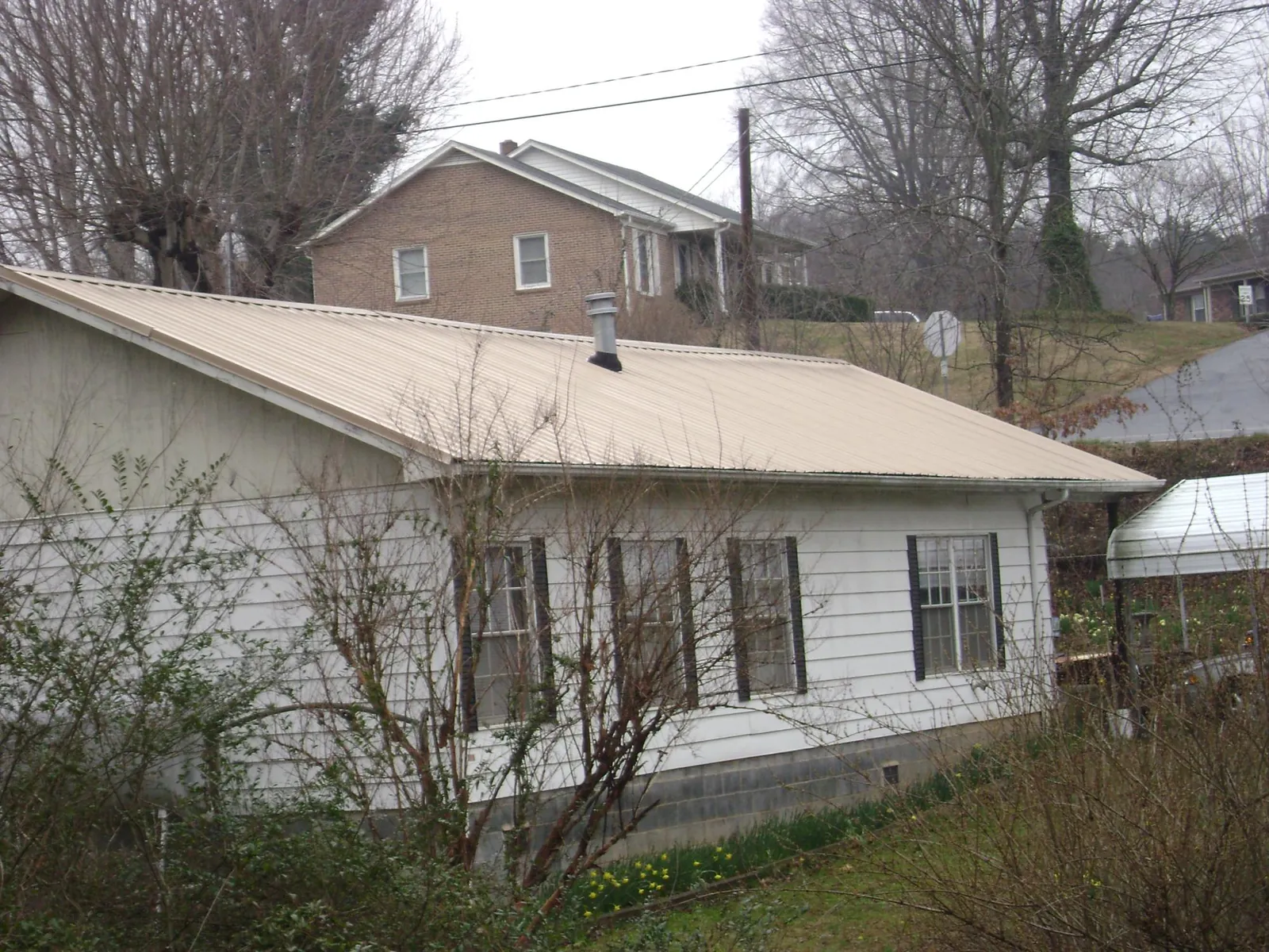 Tan metal roof on a white sided house set into a hillside — Commercial Roofing by Roofing Brothers in Crystal City